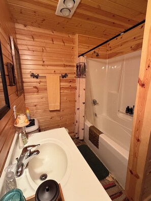 Ein kleines Badezimmer in einer Holzhütte mit Waschbecken, Spiegel und Duschbereich.