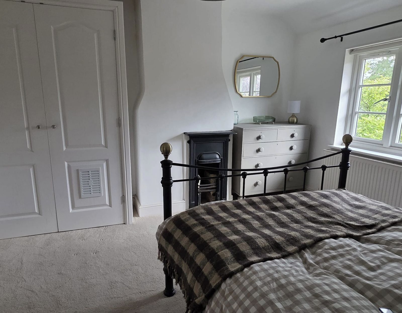 Ein Schlafzimmer mit Bett, Kommode, Spiegel, Fenster und Tür.