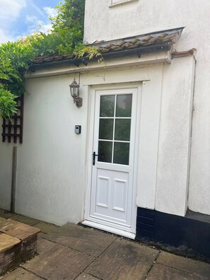 A white door with a window, a small outdoor light fixture, and a wooden fence. - A cosy Suffolk cottage in Honington. (Honington)