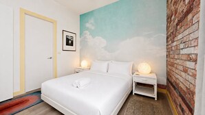 Una habitación de hotel con cama, mesita de noche, un mural en la pared y una pared decorada con ladrillos.