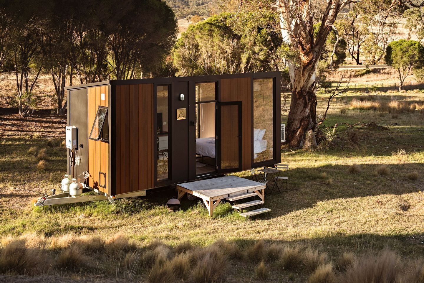 Uma cabana pequena e moderna com fachada de madeira, uma cama no interior e uma pequena área de deck.