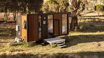 Uma cabana pequena e moderna com fachada de madeira, uma cama no interior e uma pequena área de deck.