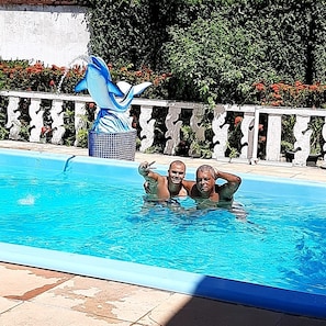 A swimming pool with a decorative dolphin statue, a tiled deck, and a white decorative fence.
