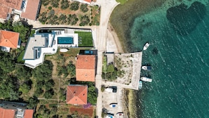 An aerial view of a coastal property with a swimming pool, multiple boats, and a beach area. - Villa Anamaria Zadarvillas (Zadar)