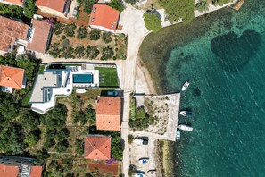 Luftaufnahme eines Küsteneigentums mit Schwimmbad, mehreren Booten und Strand.