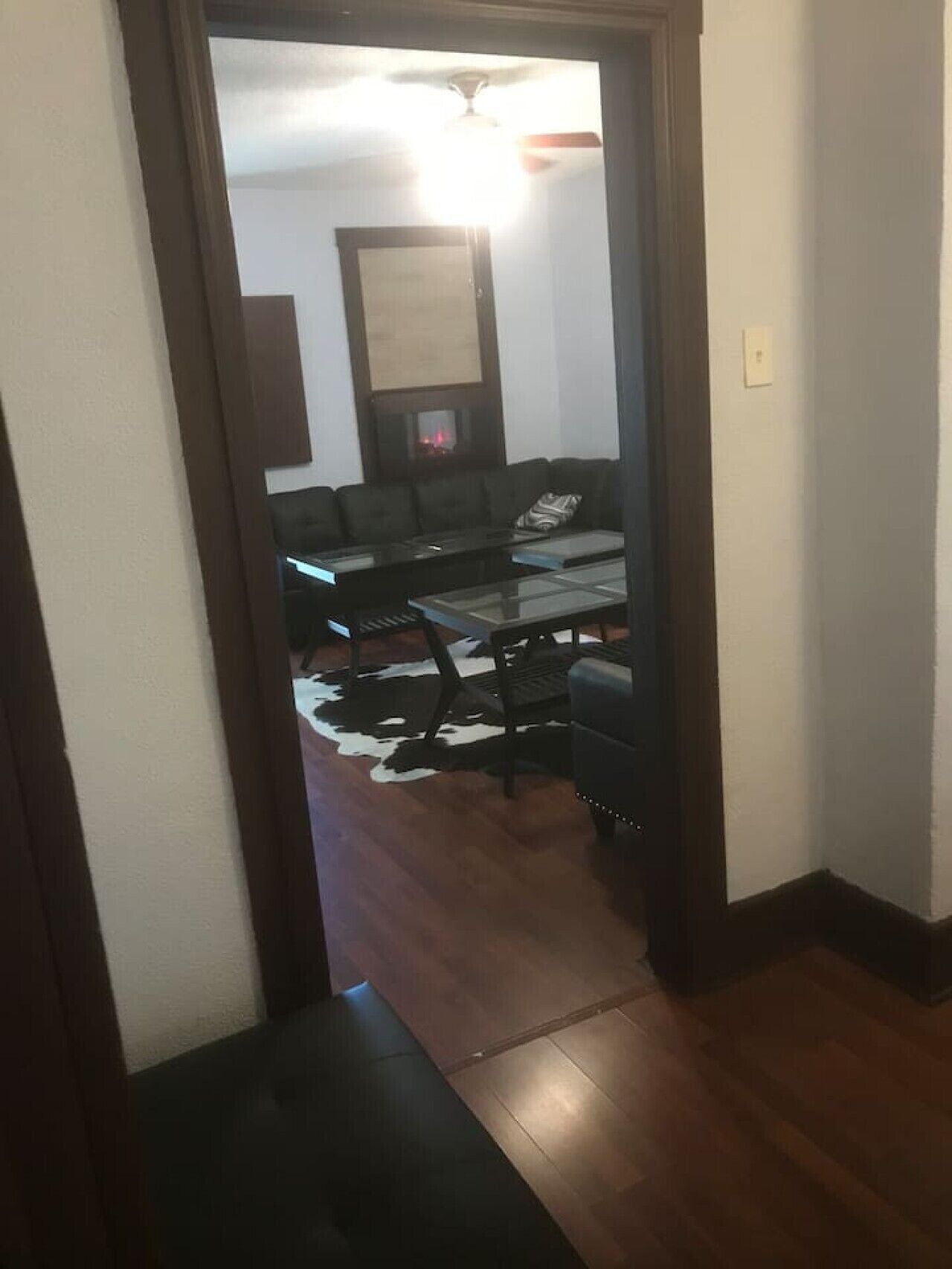 Ein Flur, der in ein Wohnzimmer mit einem schwarzen Ledersofa, einem Glastisch und einem Kuhfellteppich führt.