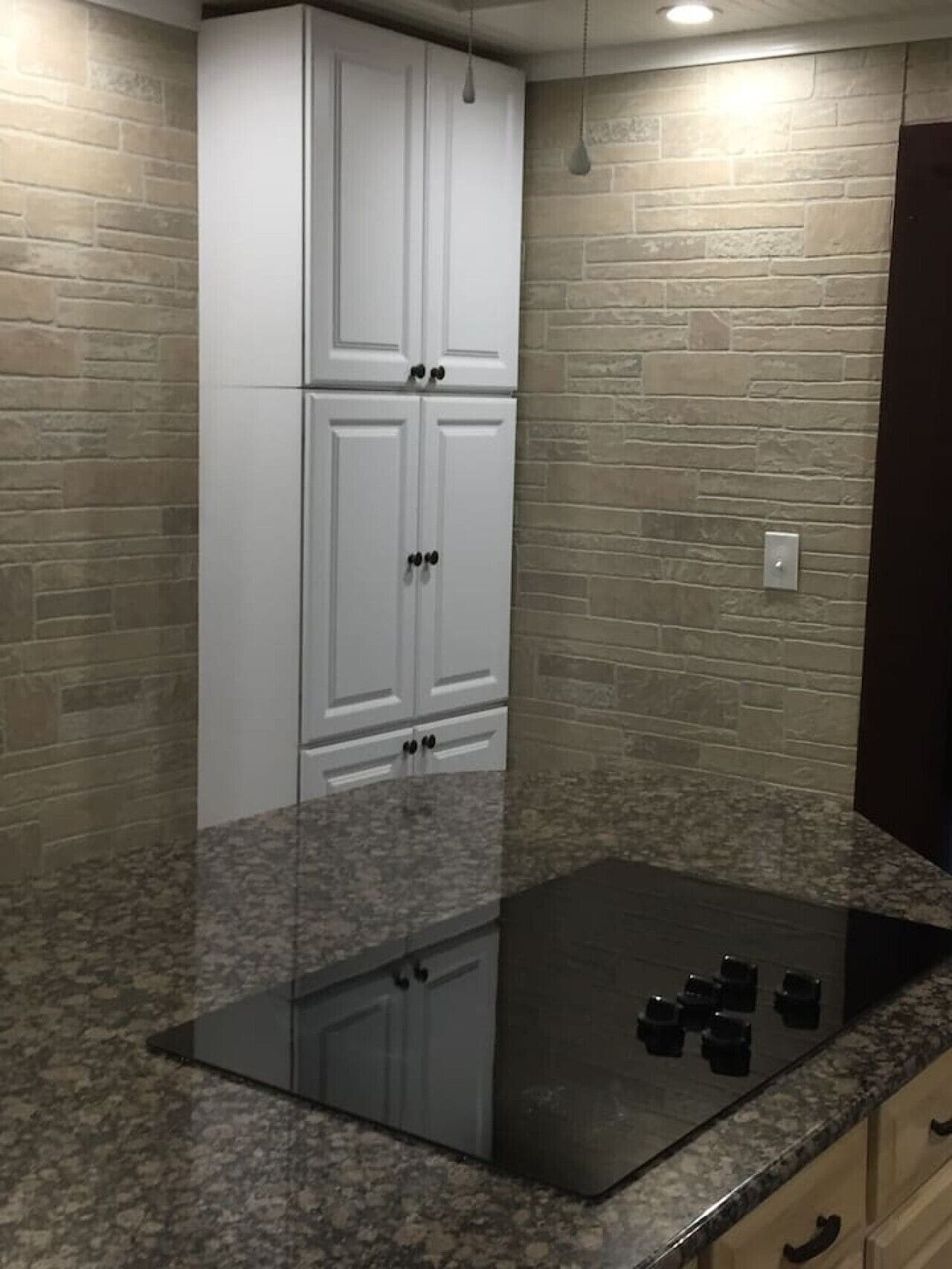 A kitchen with a granite countertop, white cabinets, and a black induction cooktop.
