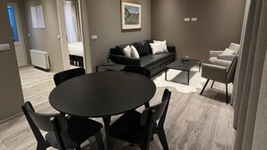 A modern living room with a round black table and chairs, a black sofa with white cushions, and a grey armchair. - Ferjukot Apartments (Sveitarfélagið Ölfus)