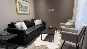 A modern living room with a black leather sofa, a white furry rug, a coffee table, and a grey armchair. - Ferjukot Apartments (Sveitarfélagið Ölfus)