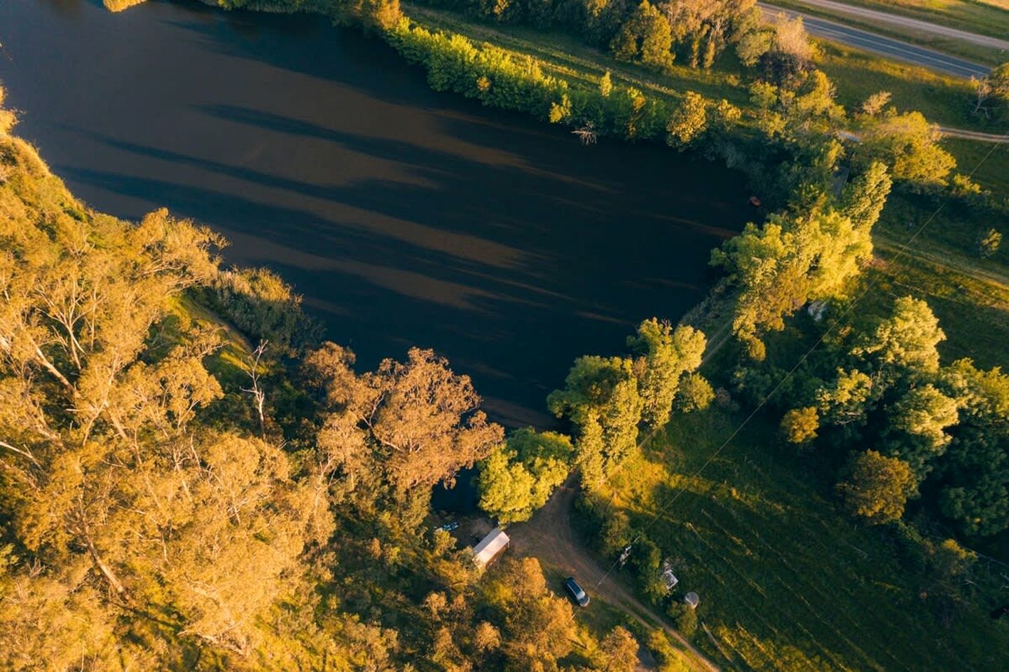 An aerial view of a river surrounded by trees and a road.