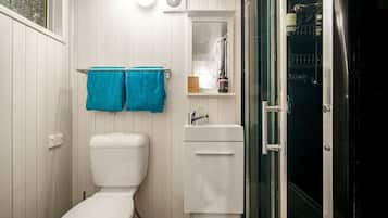 Baño pequeño con inodoro, lavamanos y cabina de ducha de vidrio.