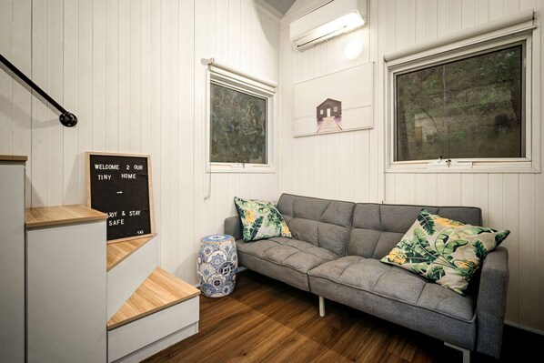 Una habitación acogedora con un sofá gris, escalones de madera, una mesita pequeña y una lámpara decorativa.