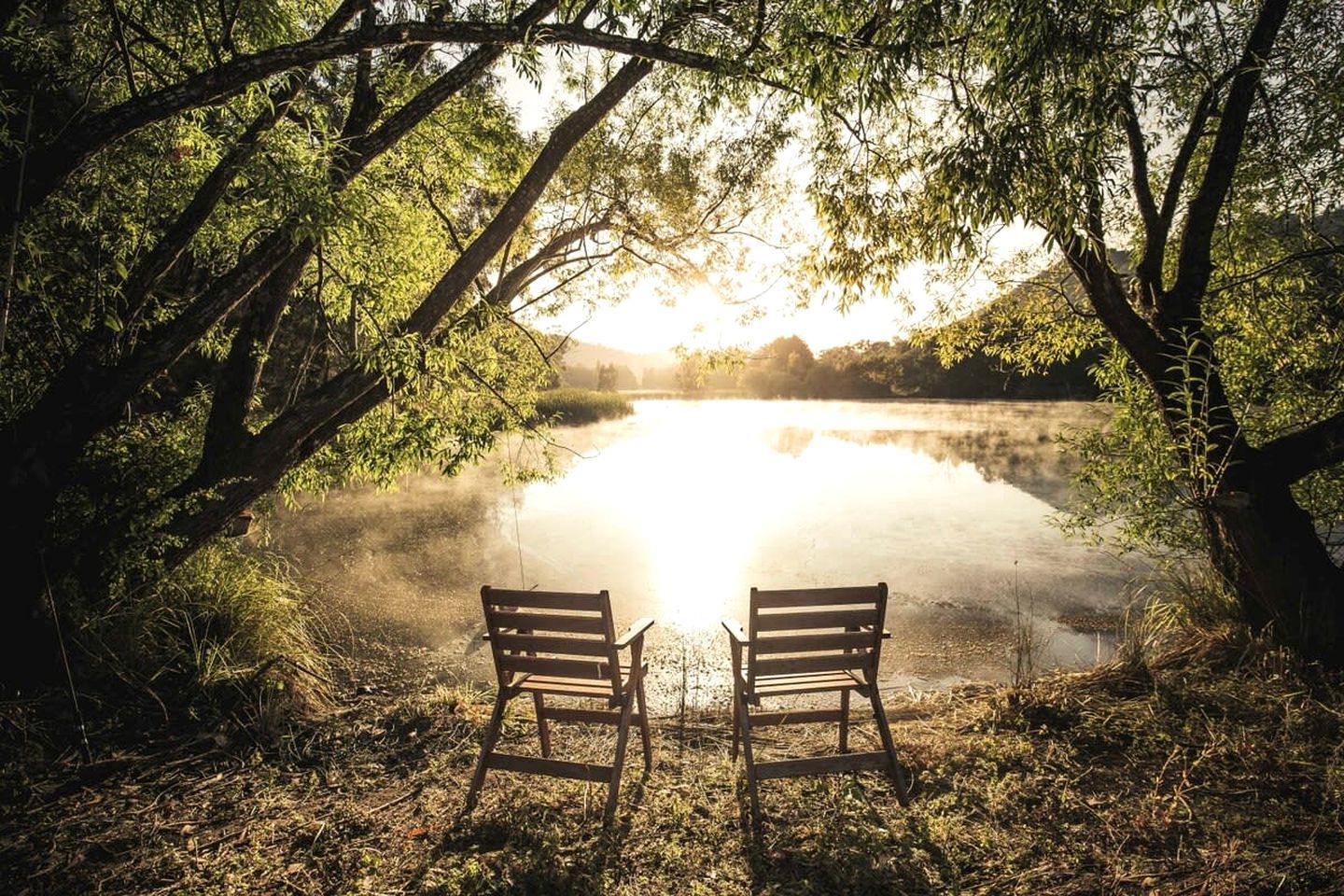 Two wooden benches facing a calm lake with trees on either side.
