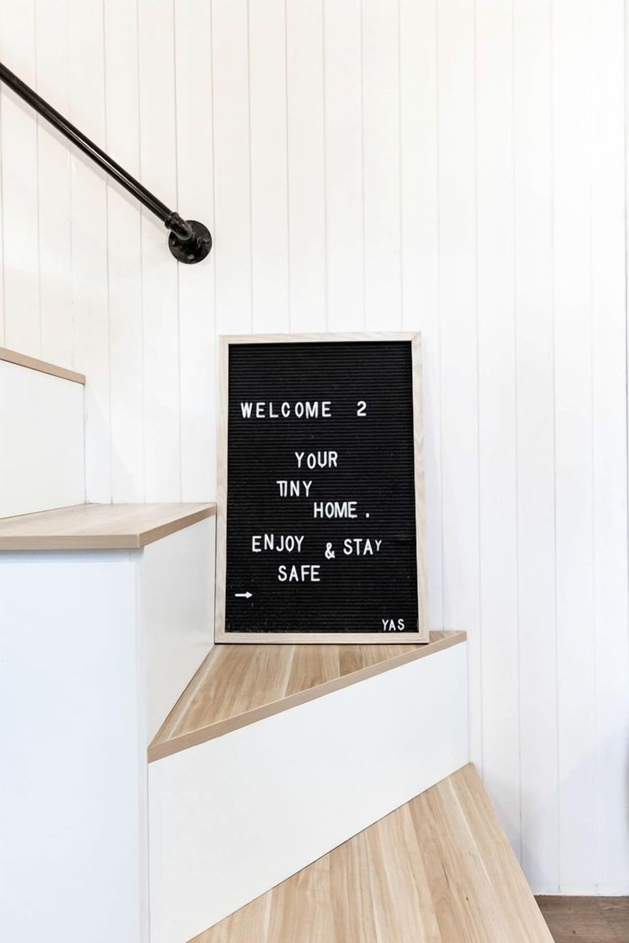 Een zwart bord met witte tekst op een witte muur, bevestigd aan een houten plank.