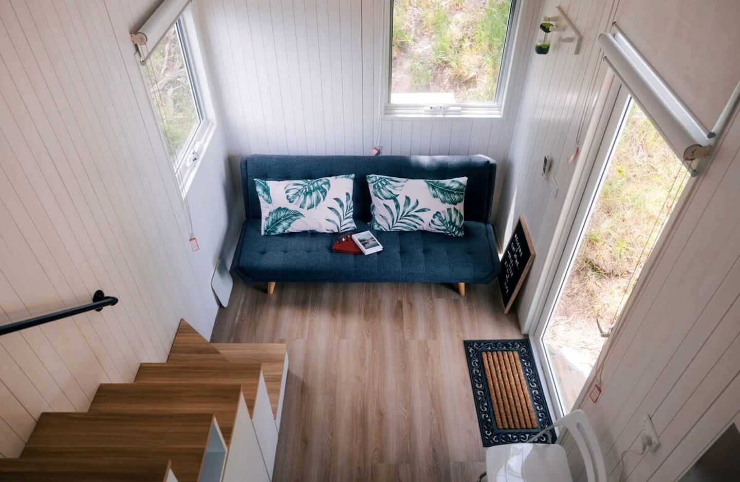 Una habitación con sofá azul, suelo de madera y ventana con vistas a zonas verdes.