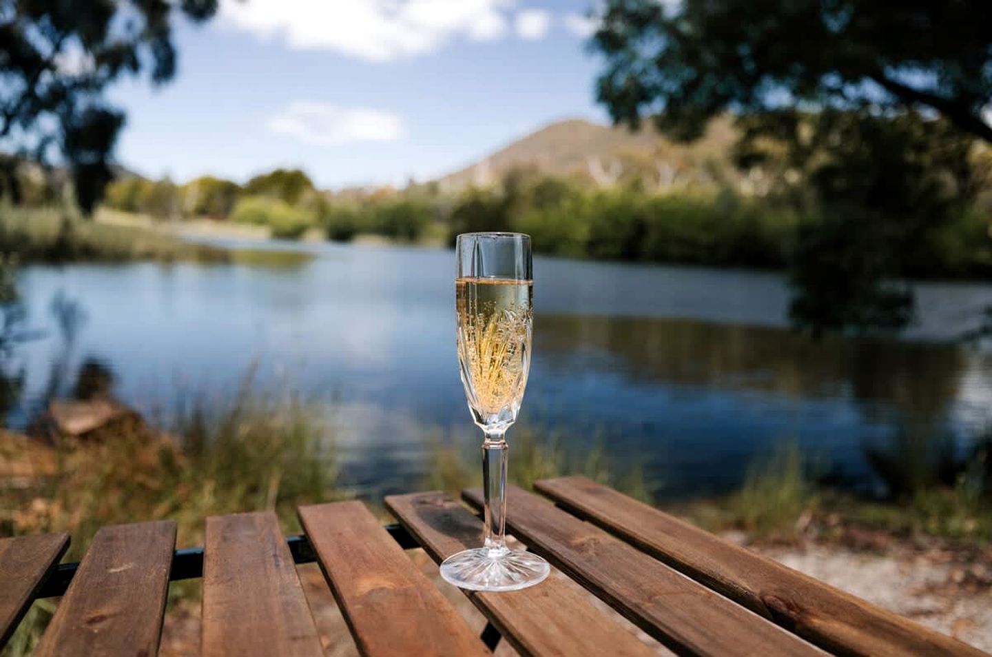 Et glas champagne på et træbord ved en sø.
