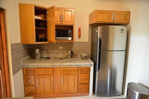 A kitchen with wooden cabinets, a stainless steel refrigerator, a microwave, and a kettle on the countertop. - Comfort Matters, the unforgettable pool, just for you (Kingston)