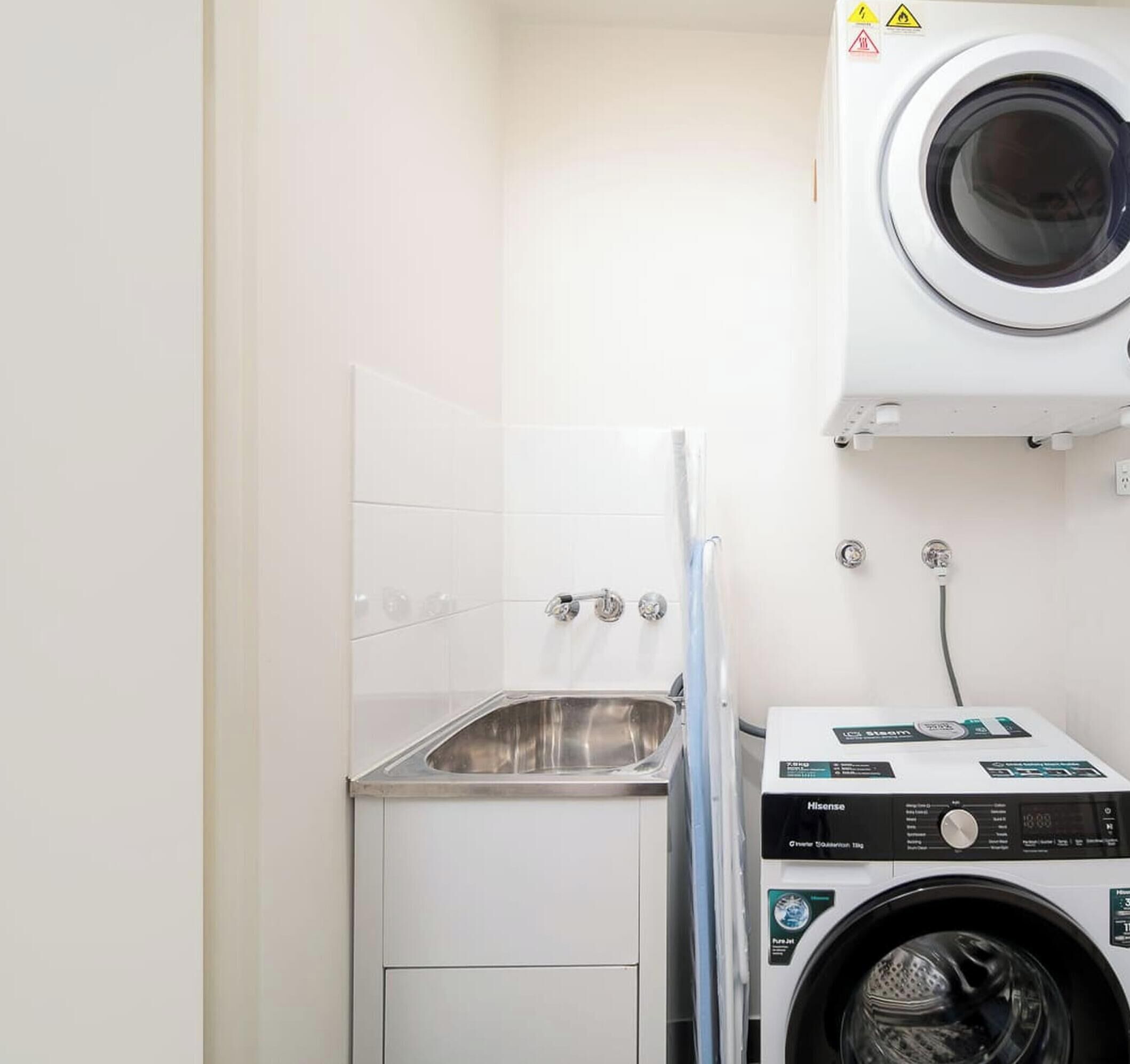 A laundry room with a washing machine, a sink, and a drying rack.