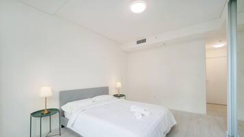 A hotel room with a bed, two bedside tables with lamps, a ceiling light, and a door leading to another room.
