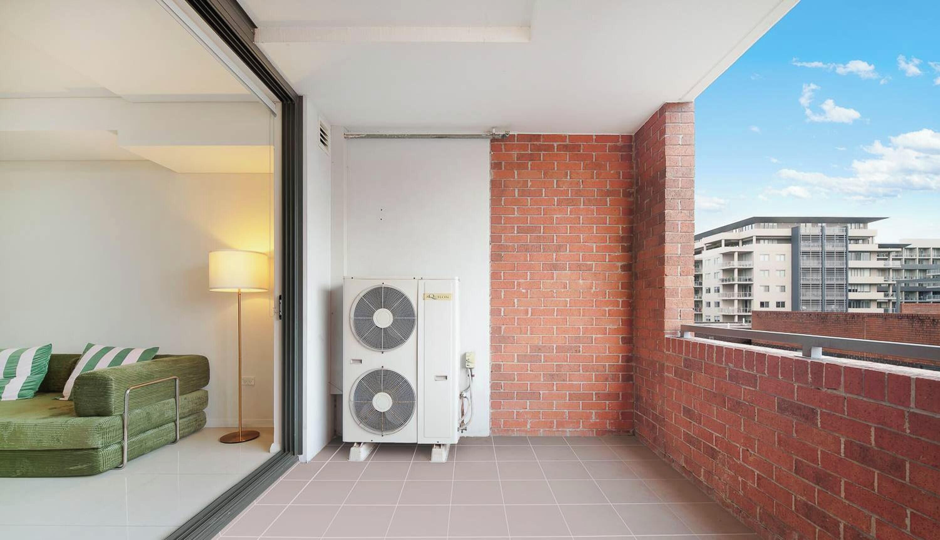 A balcony with a red brick wall, a white door, and two air conditioning units.