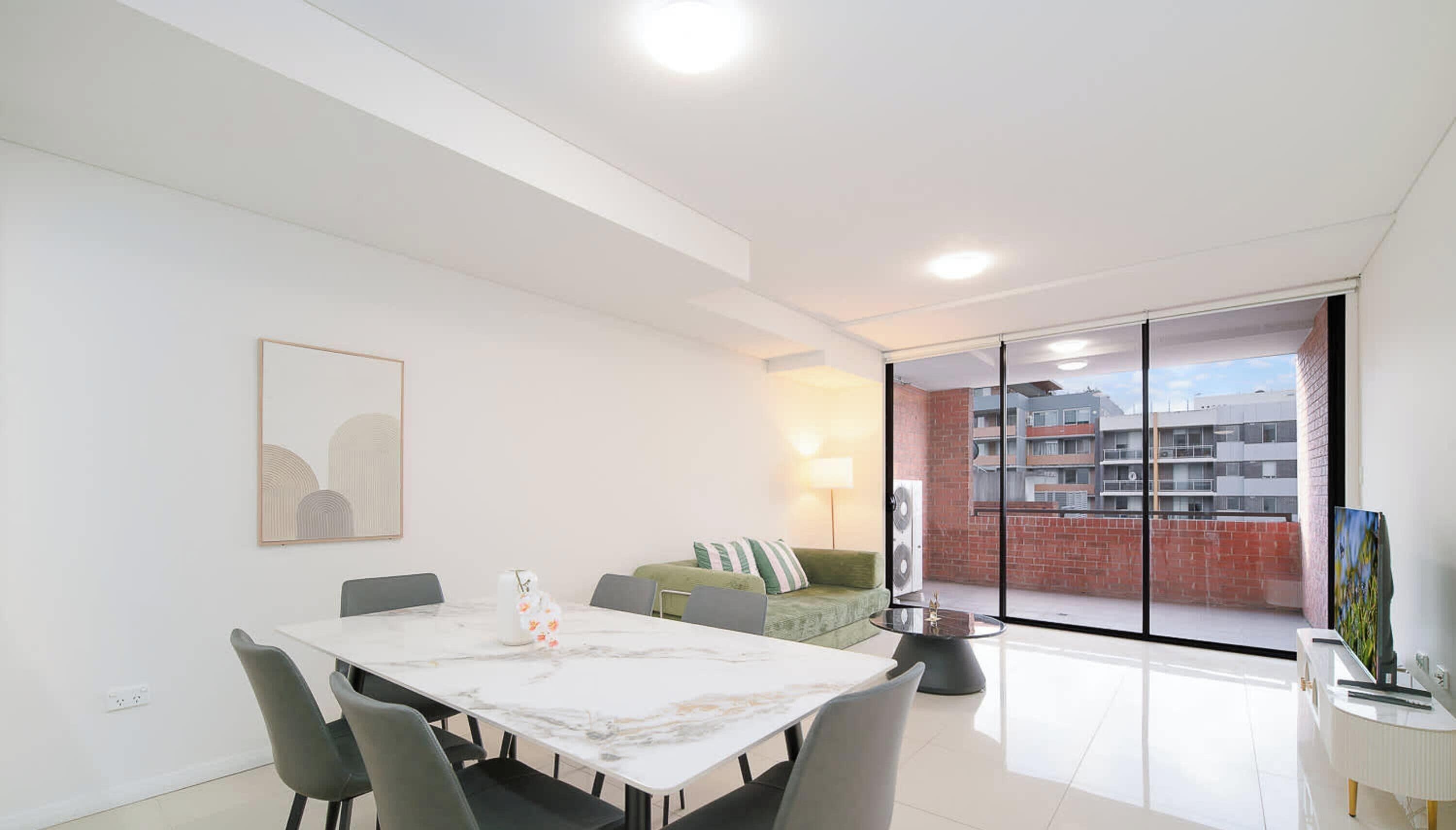 A modern living room with a dining table, chairs, a sofa, and a glass partition.