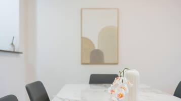 Ein Esstisch mit Stühlen, eine Vase mit Blumen und ein gerahmtes Kunstwerk an der Wand.