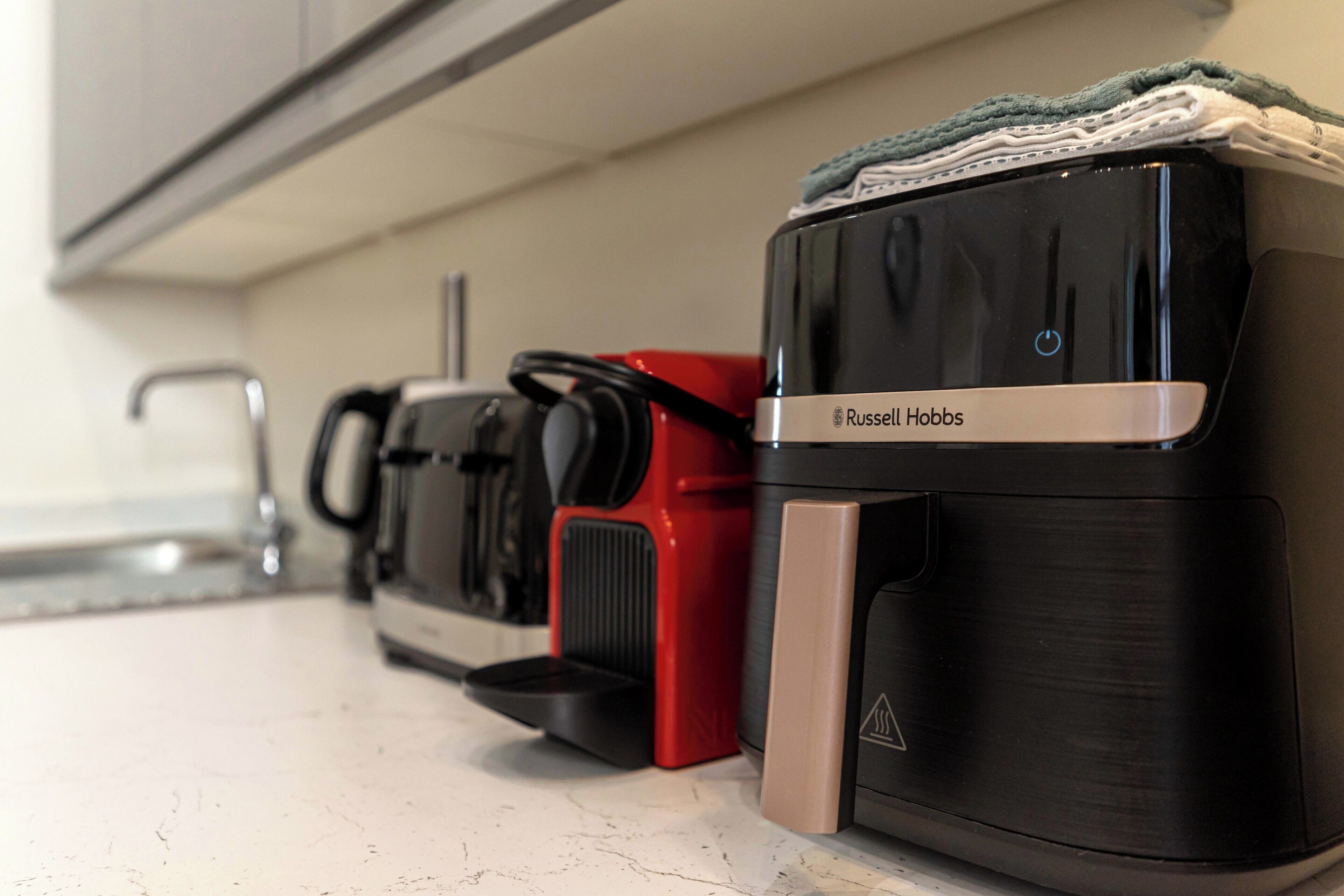 Una cocina con una cafetera, un electrodoméstico rojo y un electrodoméstico negro con una etiqueta.