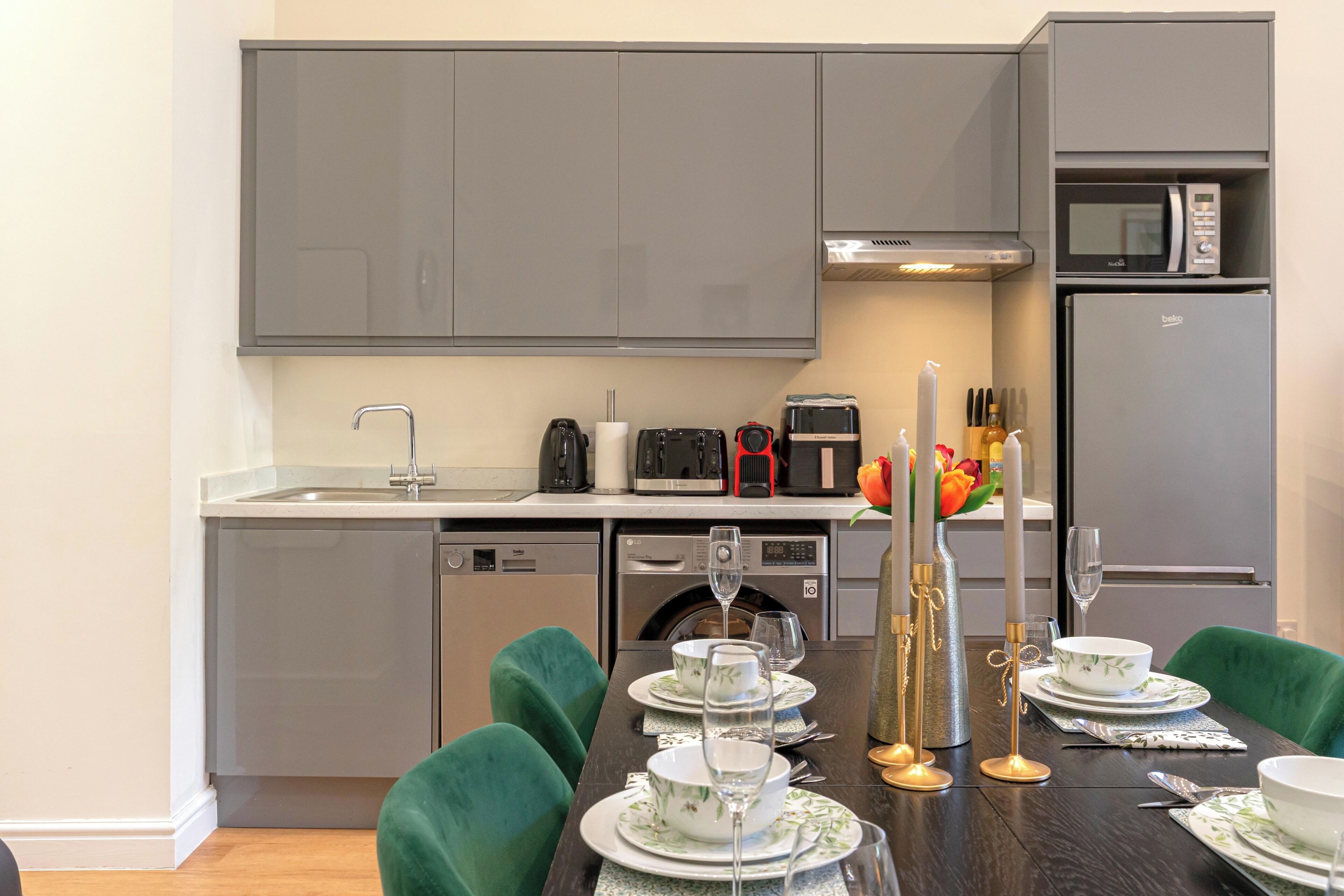 A modern kitchen with grey cabinets, a built-in microwave, a dishwasher, and a dining area with a table set for four.