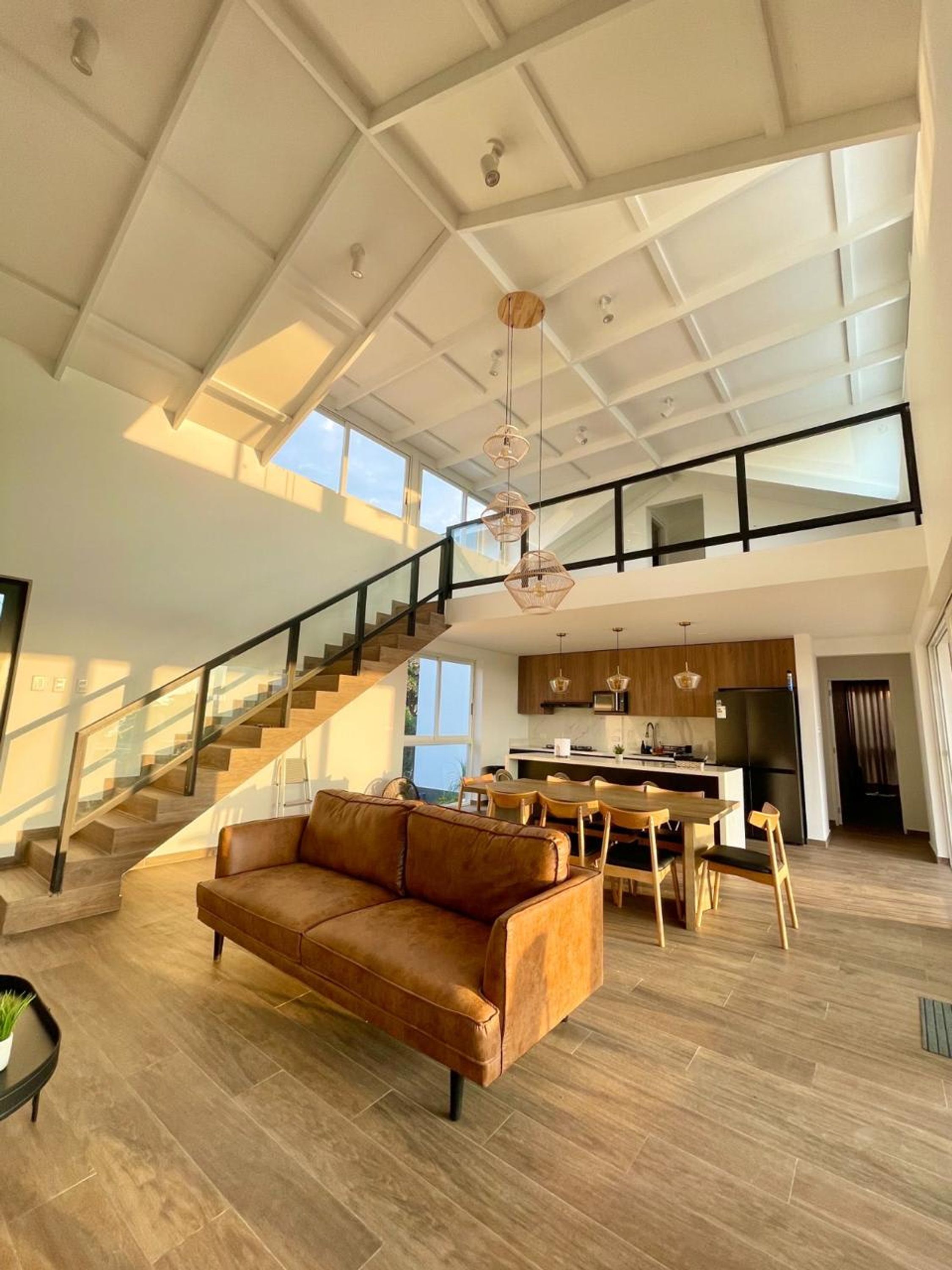 A spacious living area with a high ceiling, a staircase, a kitchen, and a dining area.