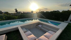 Un área de piscina moderna al aire libre con cielo iluminado, una zona de estar integrada con cojines y vistas del paisaje circundante.