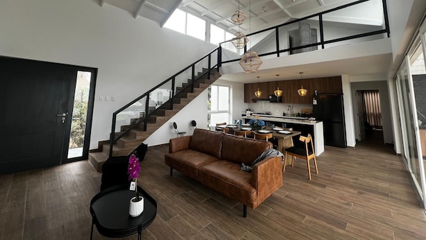 Amplia sala de estar con techo alto, una escalera que conduce a un nivel superior y una cocina moderna.