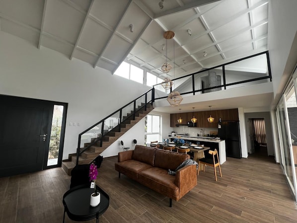 A spacious living area with a high ceiling, a staircase leading to an upper level, and a modern kitchen.