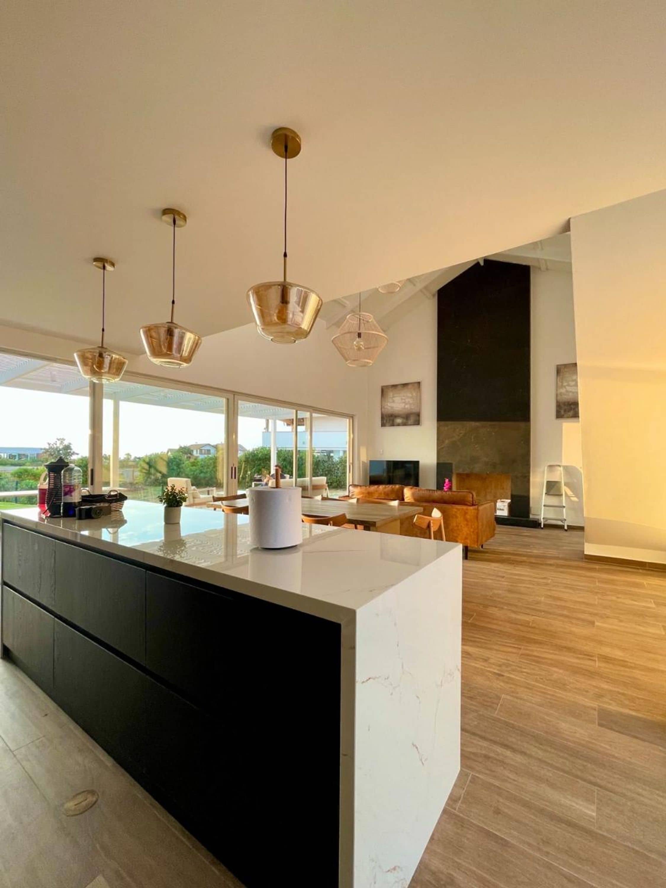 A spacious living area with a large island, modern pendant lights, and a view of the outdoors.