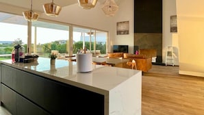 Un amplio salón con una isla grande, modernas lámparas colgantes y vistas al exterior.