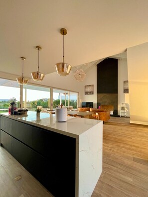 A spacious living area with a large island, modern pendant lights, and a view of the outdoors.