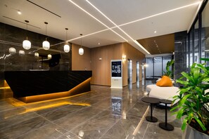 A modern hotel lobby with a marble reception desk, a seating area with a sofa and a small table, and a large window providing a view of the outside. - w Chic 2BR w Balcony AC in San Francisco (Panama City)
