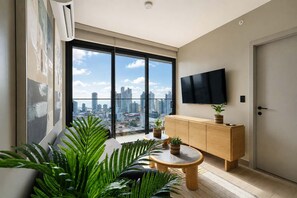 A modern living room with a large window, a flat-screen TV, a wooden cabinet, and a round coffee table. - w Chic 2BR w Balcony AC in San Francisco (Panama City)