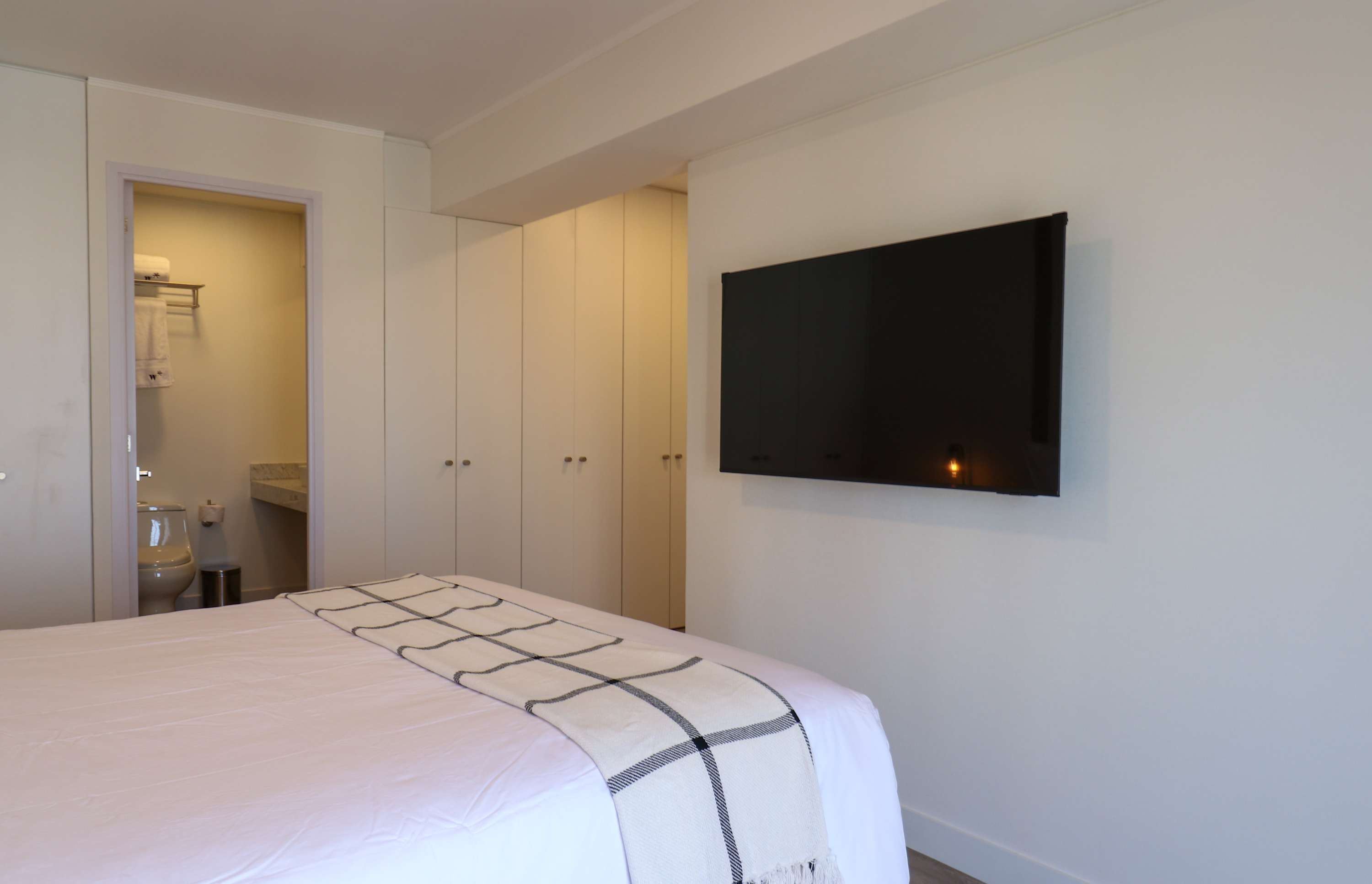A bedroom with a bed, a TV mounted on the wall, and a wardrobe.