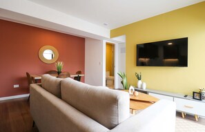 A modern living room with a sofa, a round mirror, a dining table with chairs, and a flat-screen TV mounted on the wall. - w Prime 2BR w Balcony in Miraflores (Lima)