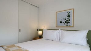 Et hotelværelse med en seng, et natbord, en lampe og et billede i ramme på væggen.