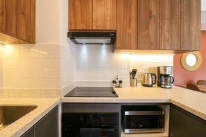 Eine Küche mit Holzausstattung, weißen Fliesen, einer Edelstahlspüle, einem Backofen, einer Mikrowelle und einer Kaffeemaschine.