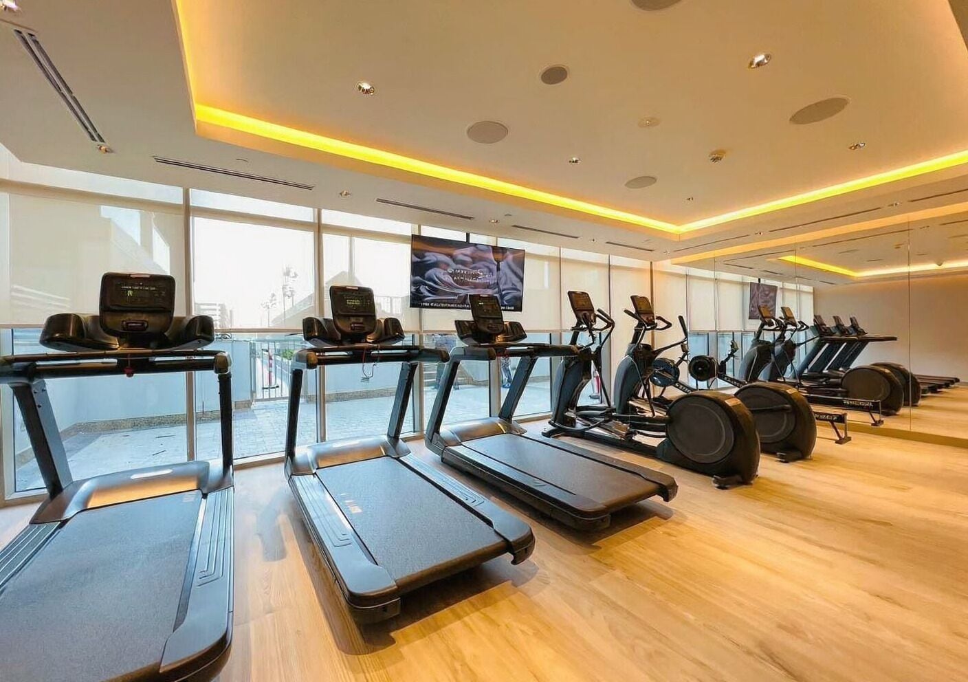 A gym with multiple treadmills, stationary bikes, and a large window providing natural light.