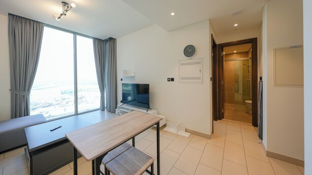 A modern hotel room with a dining area, a TV, a clock, and a shower area. - Sobha Creek Vistas Reserve Tower A (Dubai)