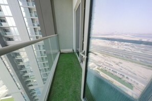 Ein schmaler Balkon mit Glastrennwand, einem kleinen Bereich künstlichem Rasen und Blick auf eine entfernte Skyline.