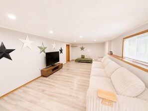 A spacious living room with a flat-screen TV, a sofa, and decorative star-shaped wall art. - The Hartford - Spacious 4-bedroom house (Des Moines)