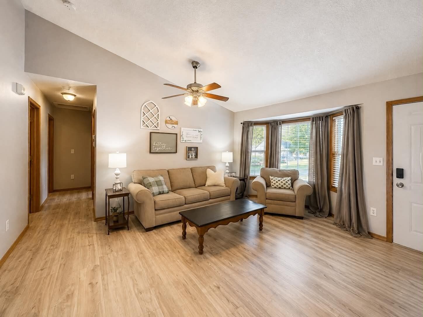 A living room with a ceiling fan, two sofas, a coffee table, and a hallway leading to another room.