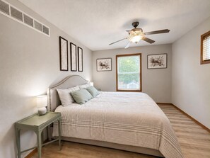 A bedroom with a bed, a nightstand, a ceiling fan, and framed artwork on the walls. - The Hartford - Spacious 4-bedroom house (Des Moines)