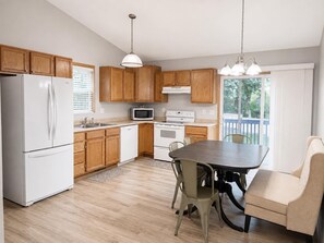 A kitchen with wooden cabinets, a white refrigerator, a microwave, an oven, a dining table with chairs, and pendant lights. - The Hartford - Spacious 4-bedroom house (Des Moines)