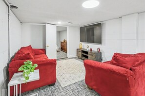 A room with two red sofas, a small white table with a green plant, a wooden cabinet, and a large TV on the wall.