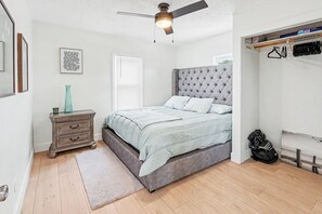 A bedroom with a bed, a dresser, a ceiling fan, a window, and a closet with hanging clothes.